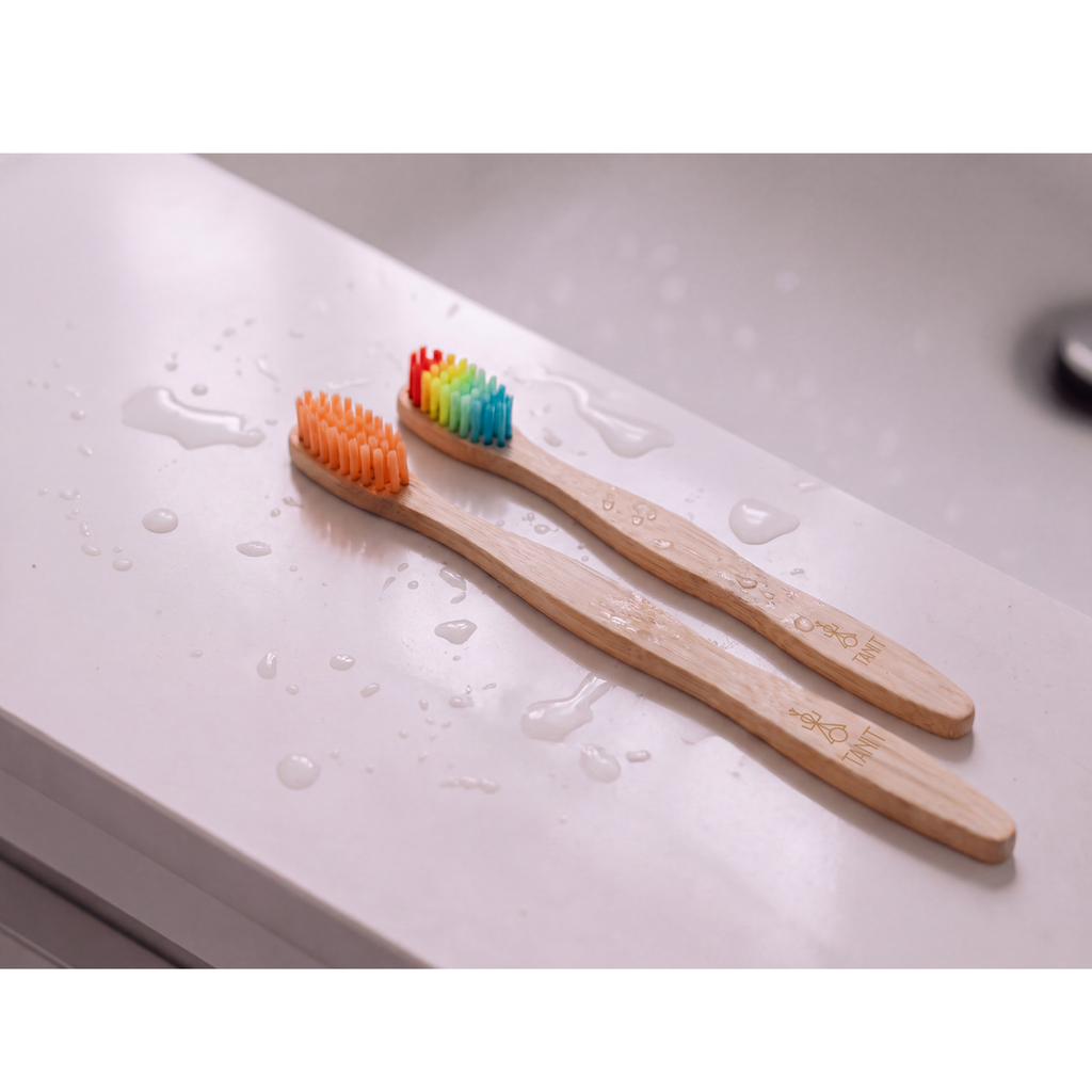 Deux brosses à dents en bambou TANIT aux soies arc-en-ciel posées sur un lavabo humide