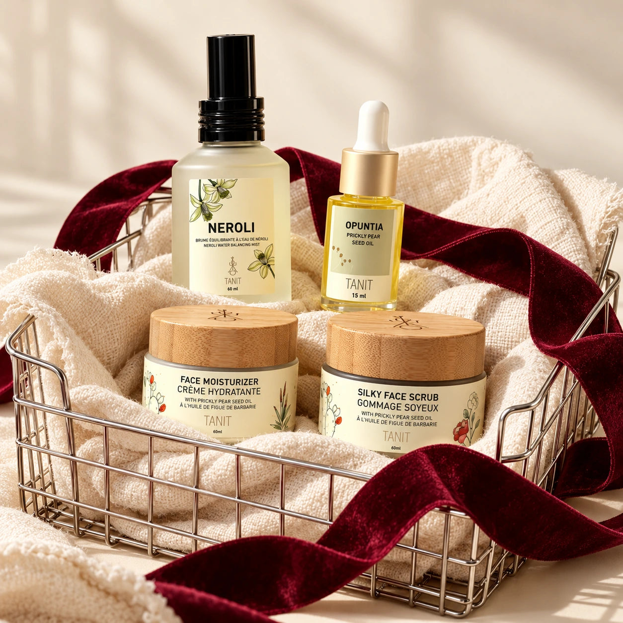 Essentiels de soins Néroli de TANIT dans un panier en métal avec du lin ivoire et un ruban bourgogne